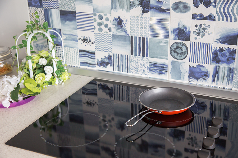 Frying pan is placed on a modern electric stove, black induction stove, cooker, hob or built in cooktop with ceramic top in Luxury kitchen interior .