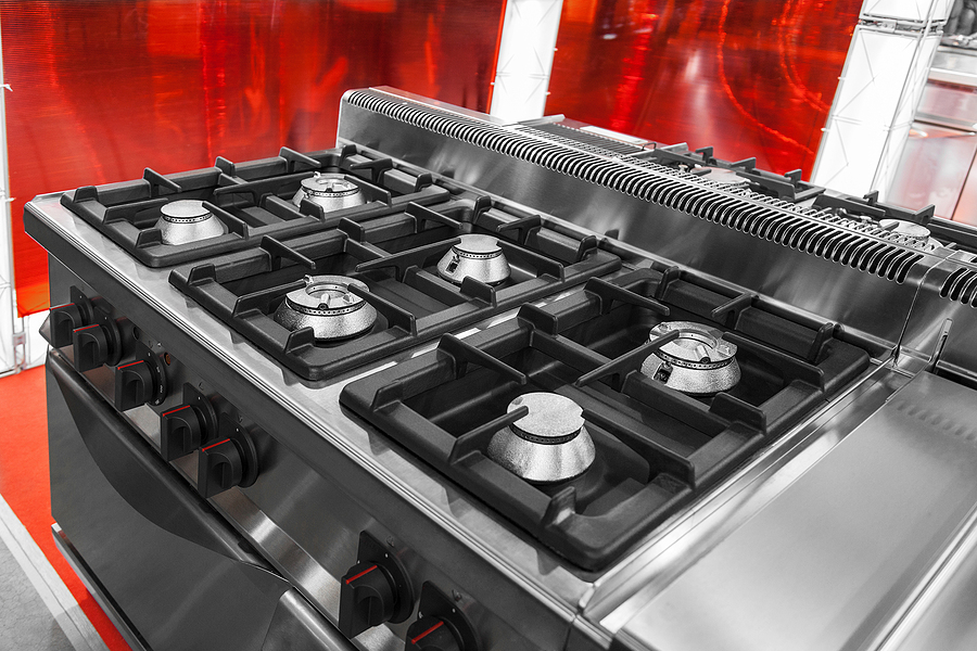 Stainless steel gas cooktop with multiple burners and black cast iron grates in a modern kitchen setting